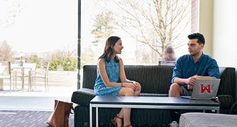 image of two students sitting on a couch, one with a laptop